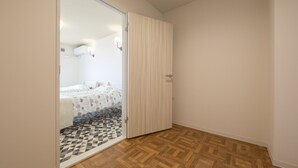 Une chambre avec un parquet en bois disposé en motif de chevron, un lit recouvert d’une couvre-lit à motifs et une porte coulissante donnant sur une autre pièce.
