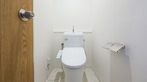 Une petite salle de bain propre, avec des toilettes blanches, une porte en bois et un mur blanc.