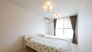 Une chambre avec deux lits, une fenêtre avec des rideaux, un appareil de climatisation et un luminaire au plafond.