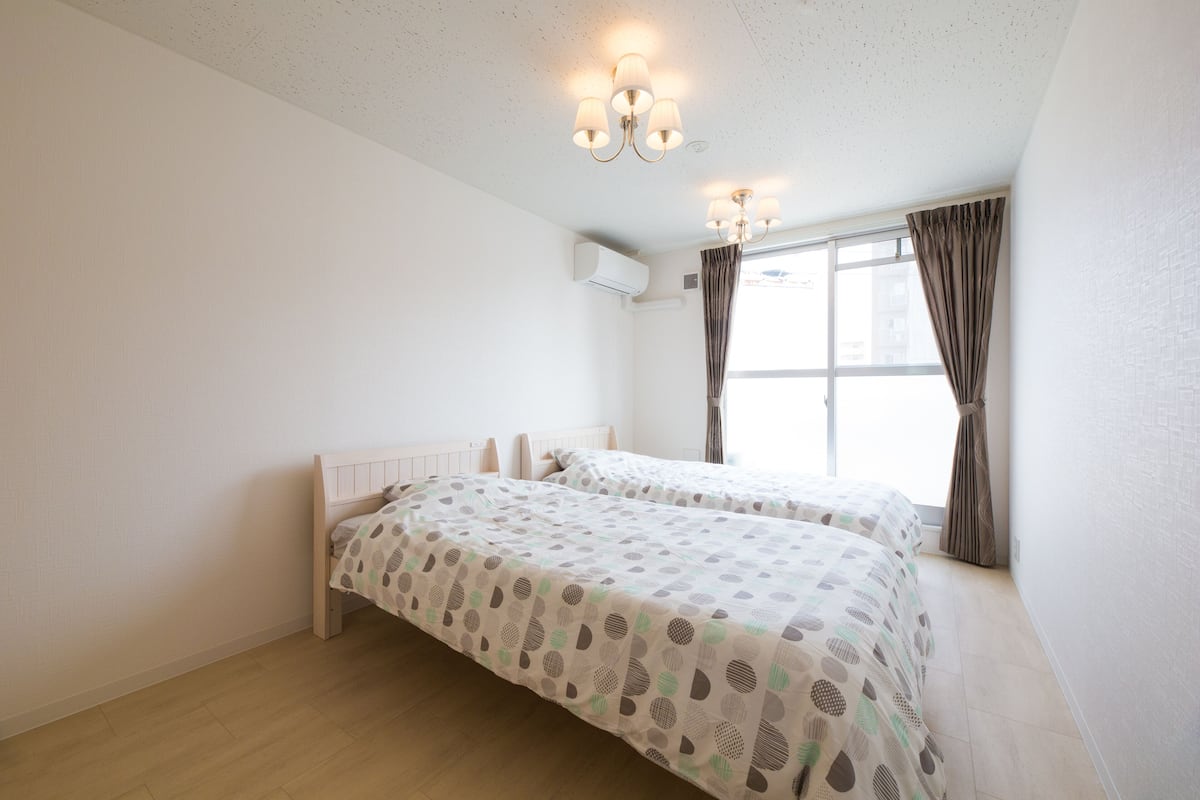 Une chambre avec deux lits, une fenêtre avec des rideaux, un appareil de climatisation et un luminaire au plafond.