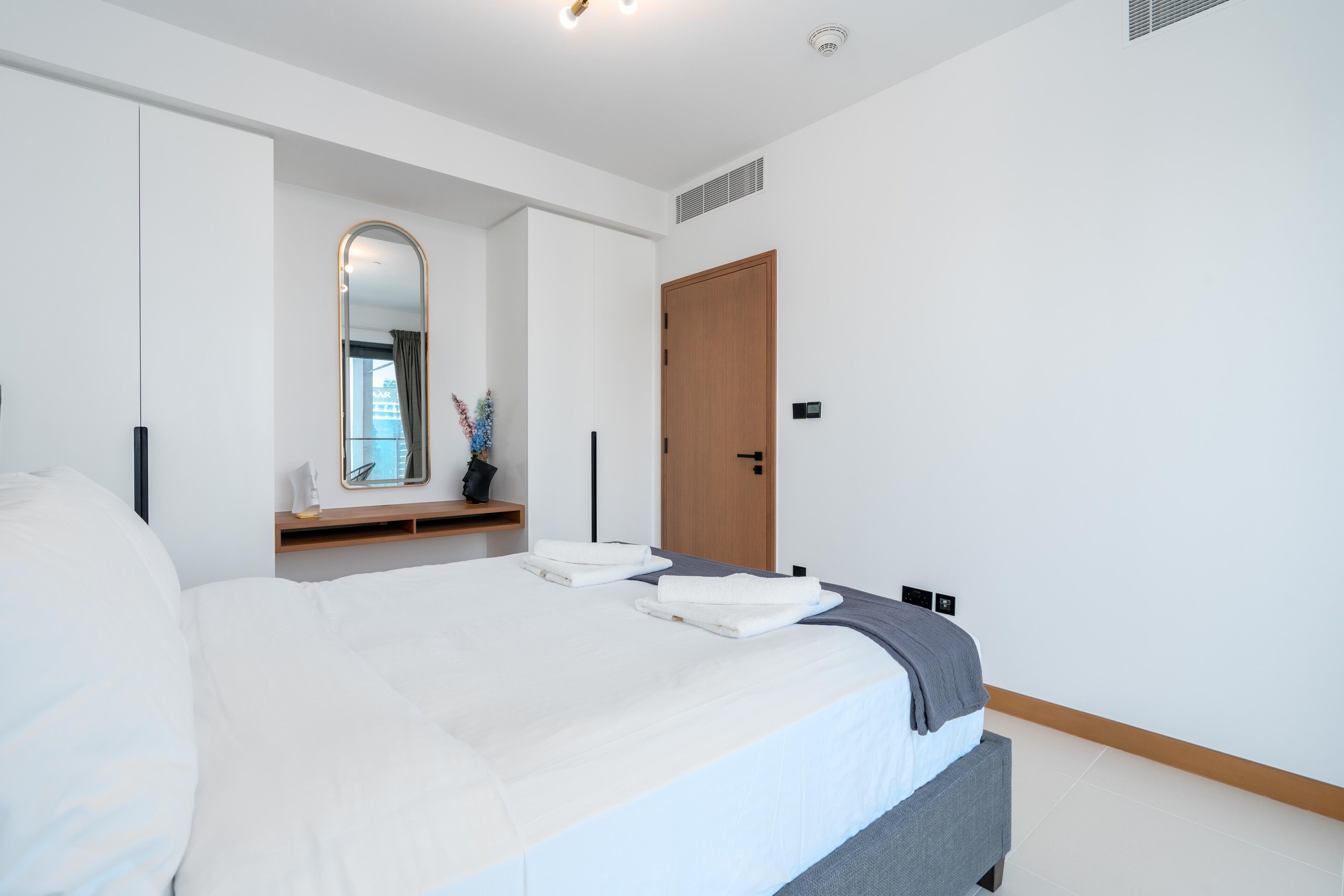 A modern bedroom with a large bed, a wooden door, and a mirror on the wall.