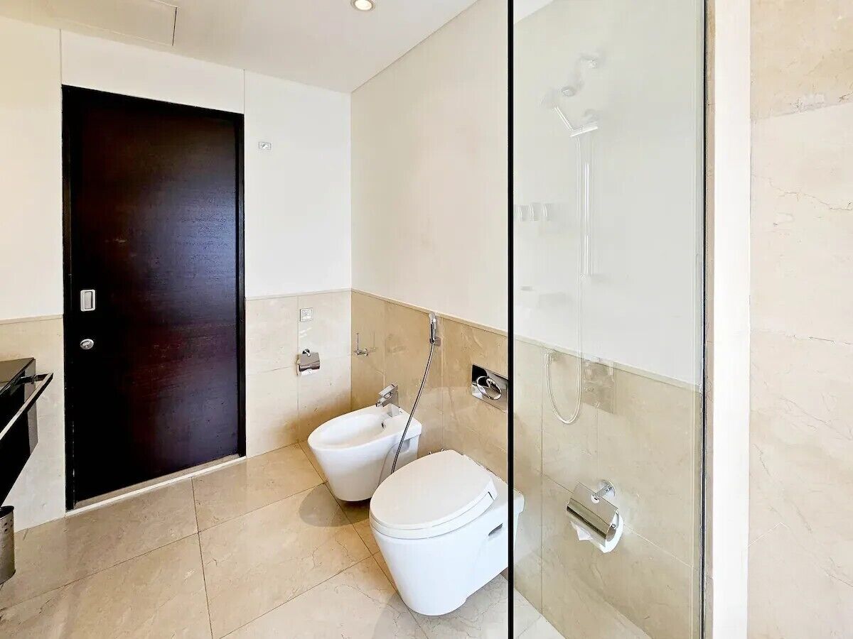 A modern bathroom with a bidet, toilet, and a glass shower enclosure.