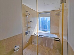 A modern bathroom with a glass shower enclosure, a bathtub, and a window offering a city view.