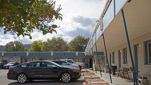 A parking area with a row of cars parked in front of a building with a blue awning. - Grand Central Motel (Ely)