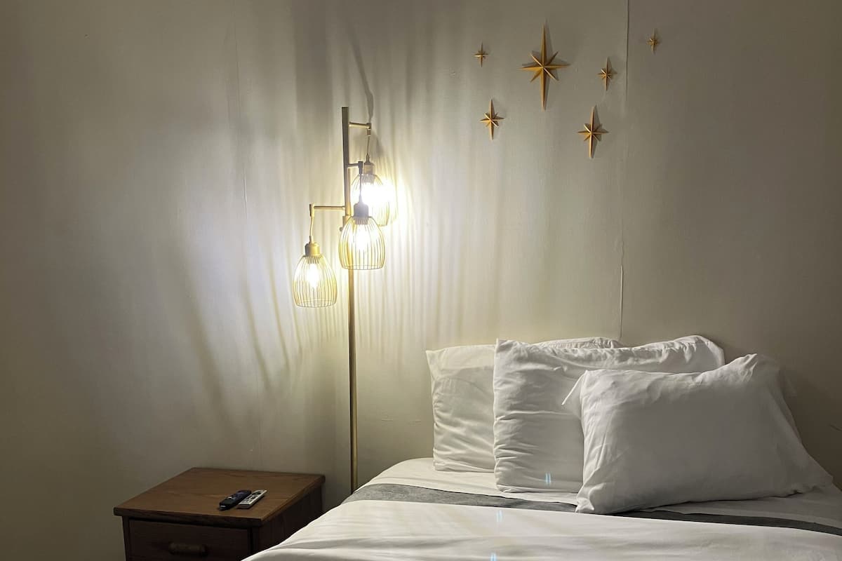 A hotel room with a bed, a nightstand, and a wall-mounted lamp.