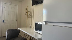 A compact kitchen with a white refrigerator, a built-in microwave, and a small dining table with a single chair. - Grand Central Motel (Ely)