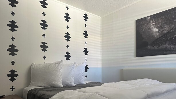 A bedroom with a bed, white bedding, a nightstand, and a wall with decorative black patterns. - Grand Central Motel (Ely)