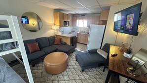 A compact living space with a sofa, ottoman, and a TV mounted on the wall. - Grand Central Motel (Ely)