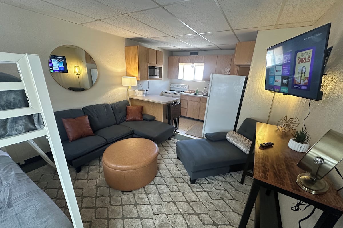 A compact living space with a sofa, ottoman, and a TV mounted on the wall.