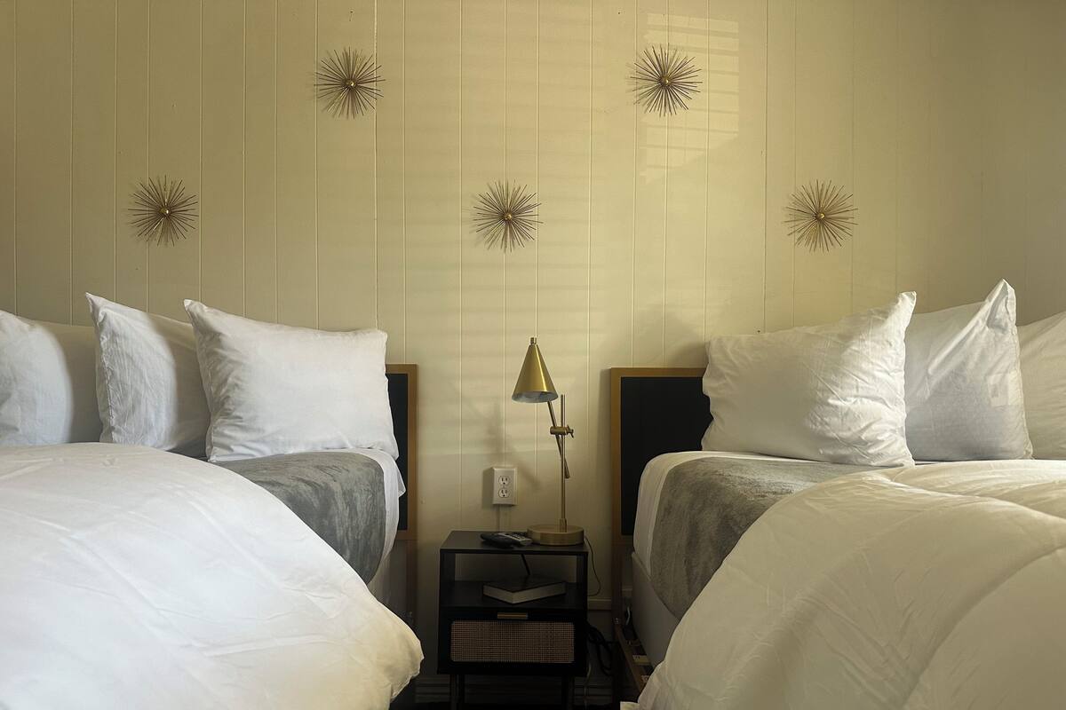 A hotel room with two beds, a nightstand with a lamp, and decorative wall sconces.