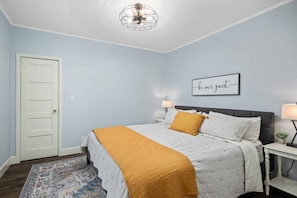 A bedroom with a bed, a nightstand, a wall-mounted lamp, a door, and a ceiling fan. - Marvelous Single Level Home in Central Newberg, Fire-Table, Covered Patio, Seven Blocks to Downtown (Newberg)