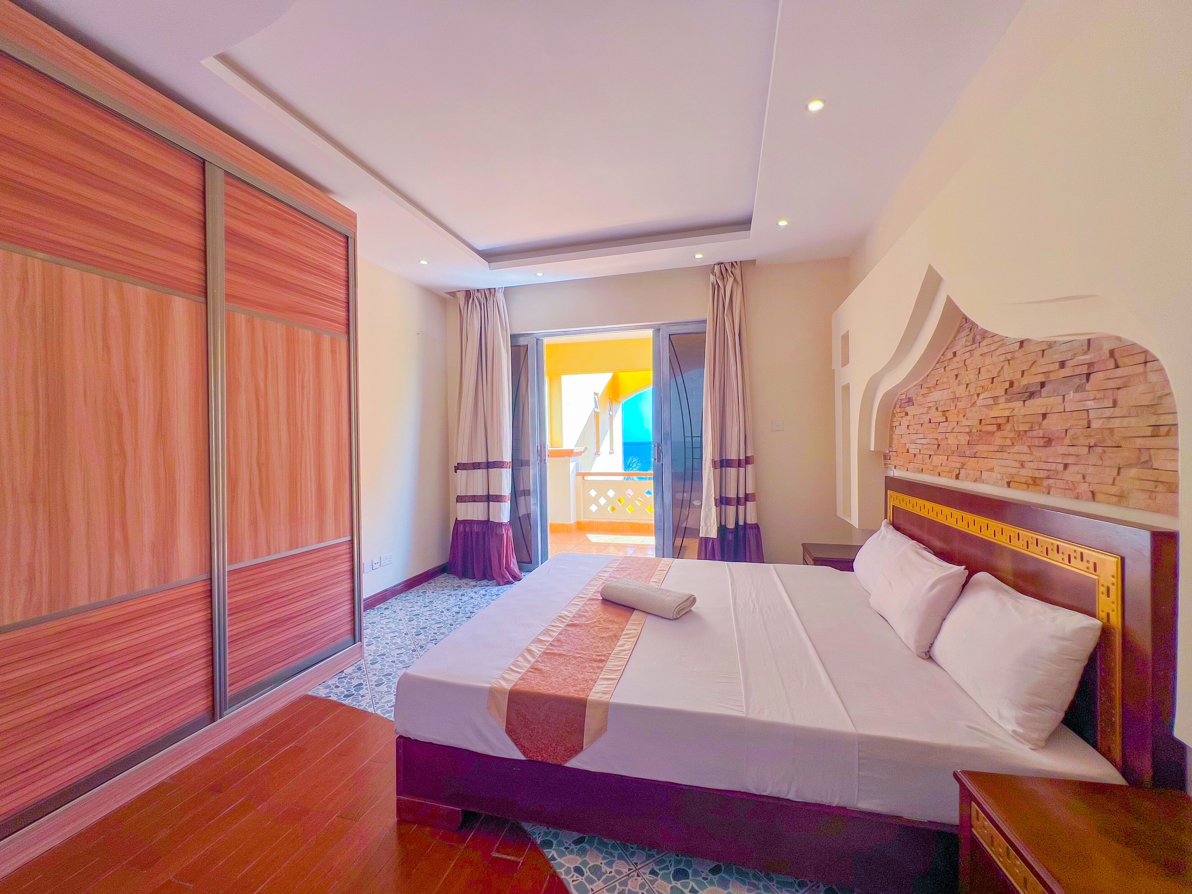 Een hotelkamer met een groot bed, een houten garderobe en uitzicht op het balkon.