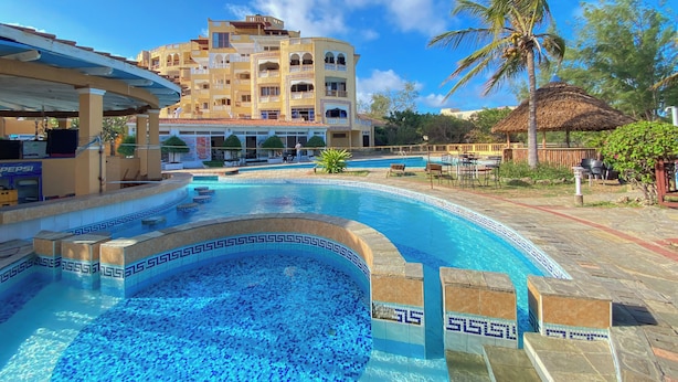 Ein Swimmingpool mit blauen Mosaikfliesen, umgeben von einer Lounge mit Gartenmöbeln und einer Struktur mit einem Reetdach.