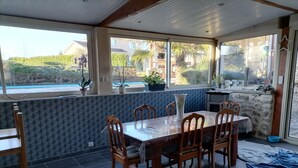 A dining area with a table and chairs, a view of the outdoors, and a stone wall. - Maison Limousine en Pierre Apparentes (Compreignac)