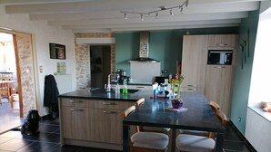 A modern kitchen with a central island, wooden cabinets, a black countertop, and a dining area with two chairs. - Maison Limousine en Pierre Apparentes (Compreignac)
