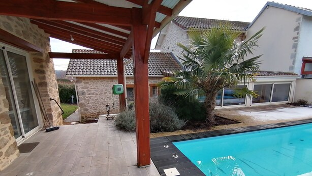 A covered patio area with a swimming pool, stone walls, and a tiled roof. - Maison Limousine en Pierre Apparentes (Compreignac)