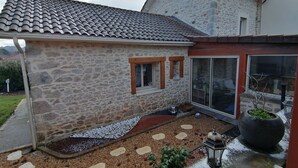 A stone house with a tiled roof, a small attached structure, and a garden with stepping stones and a lantern. - Maison Limousine en Pierre Apparentes (Compreignac)