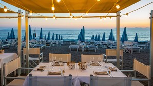 A beachside restaurant with tables and chairs under a canopy, overlooking the sea. - Residence Stella Marina (Cecina)