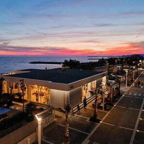 A modern building with a glass facade, a sign reading "BEACH", and a view of the sea at sunset. - Residence Stella Marina (Cecina)
