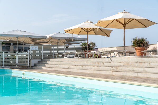 A swimming pool with multiple beige umbrellas and lounge chairs. - Residence Stella Marina (Cecina)