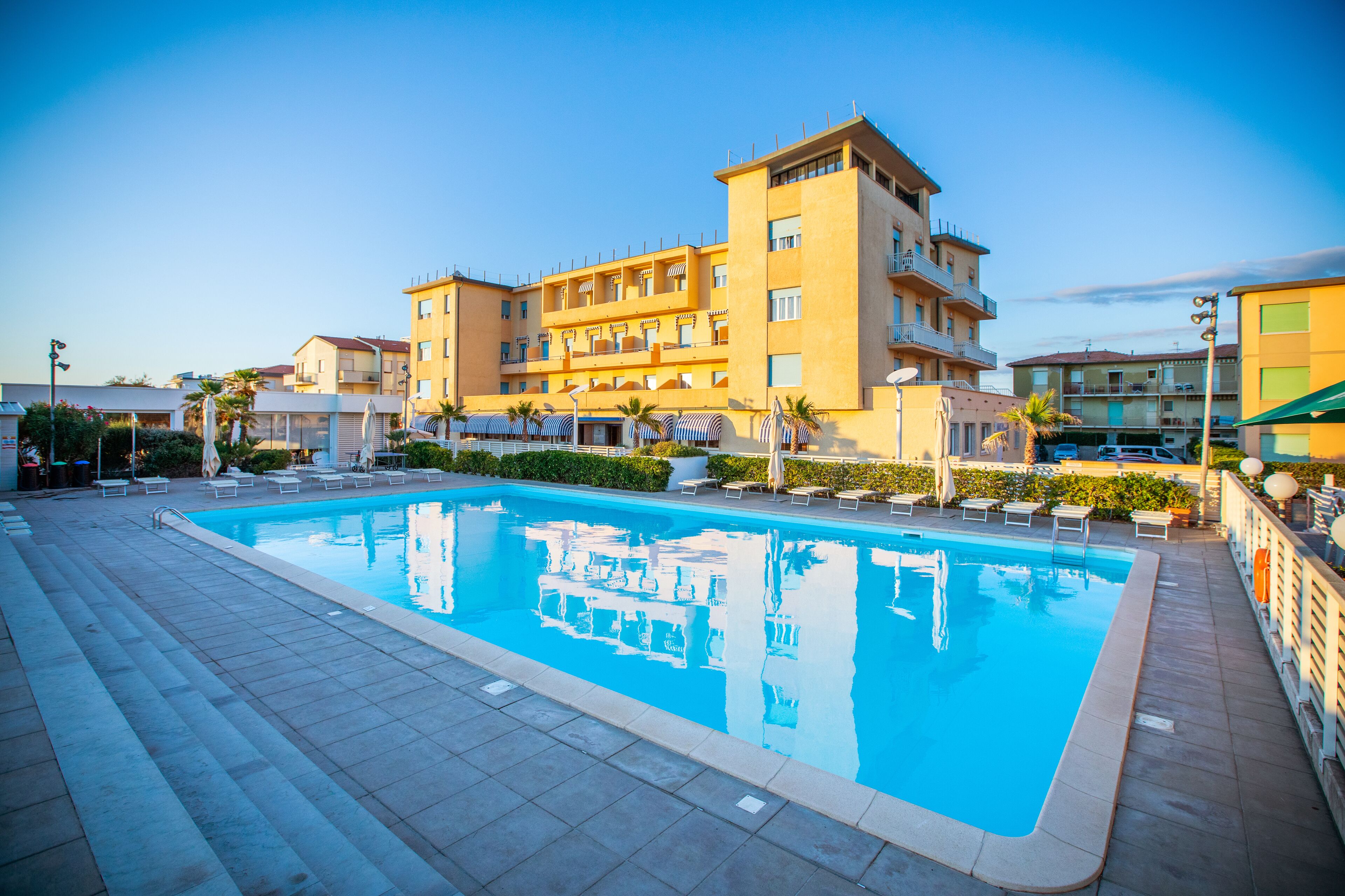 Piscina com espreguiçadeiras e um edifício com varandas ao fundo.