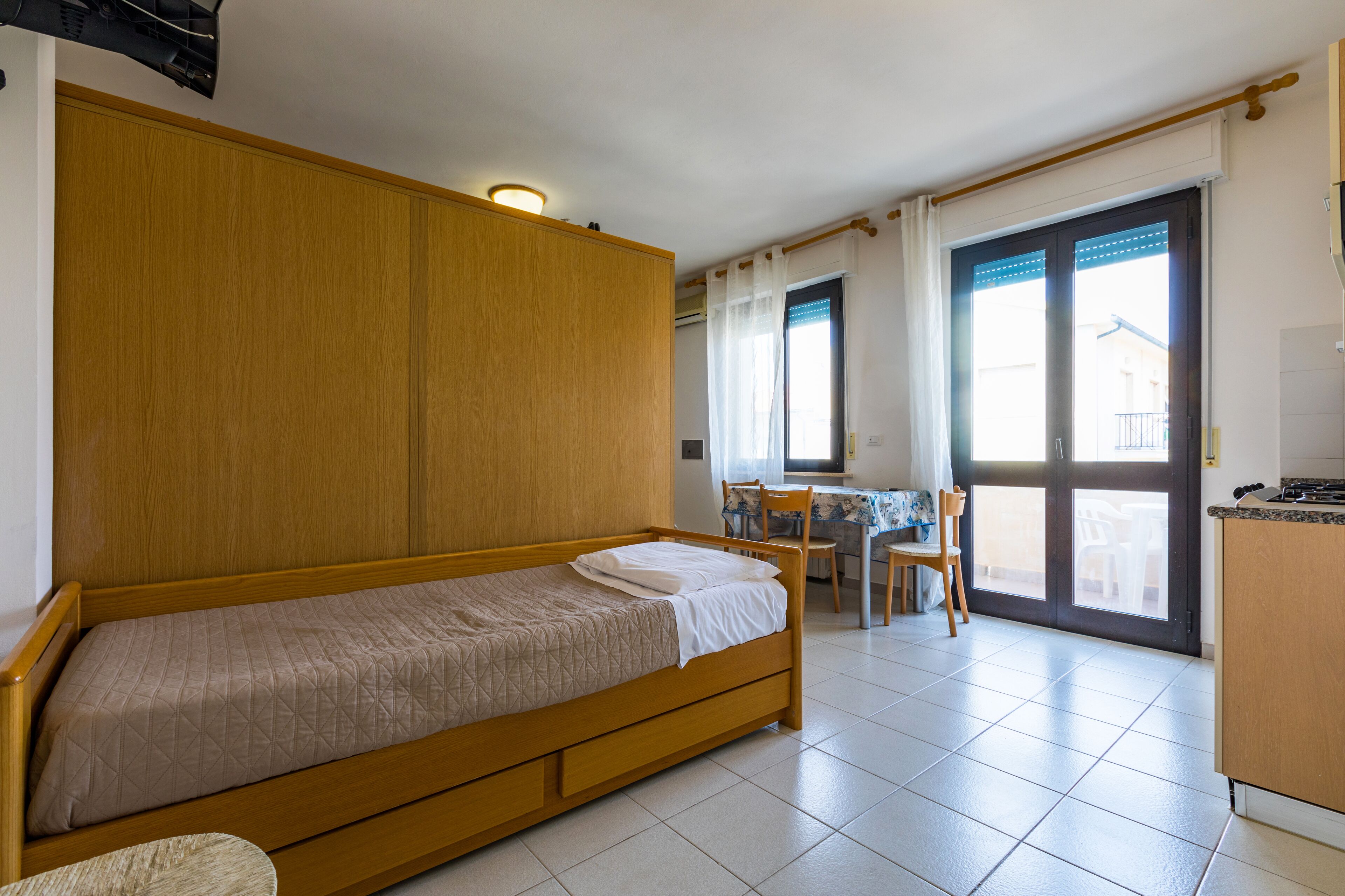 Een kamer met een houten bed, een eettafel met stoelen en een keukenhoek.