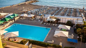 A pool area with lounge chairs and umbrellas, a beach with umbrellas and chairs, and a rocky breakwater. - Residence Stella Marina (Cecina)