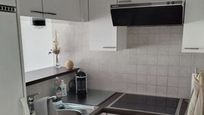 Una cocina compacta con armarios blancos, una encimera negra, horno integrado y pileta de acero inoxidable.