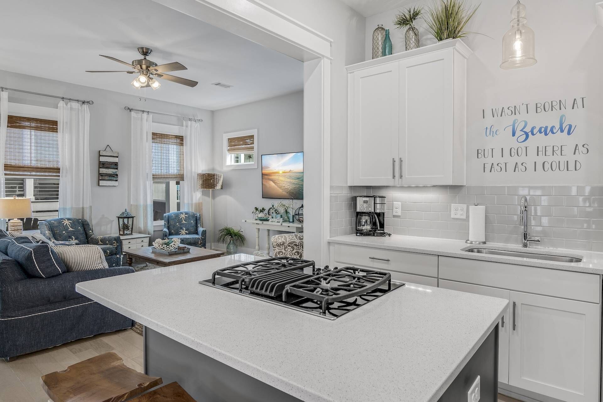 A modern kitchen with white cabinetry, a central island with a gas stove, and a dining area with a sofa and a coffee table.