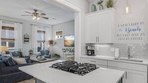 Une cuisine moderne avec des meubles blancs, un îlot central doté d’une cuisinière à gaz et un coin repas comprenant un canapé et une table basse.