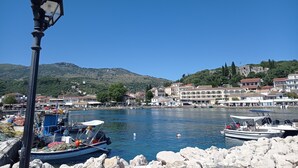 A coastal town with a clear blue sky, a historic building with a flag, boats docked at the harbor, and a street lamp in the foreground. - Solaris Methea Deluxe Suites  (Kassiopi)