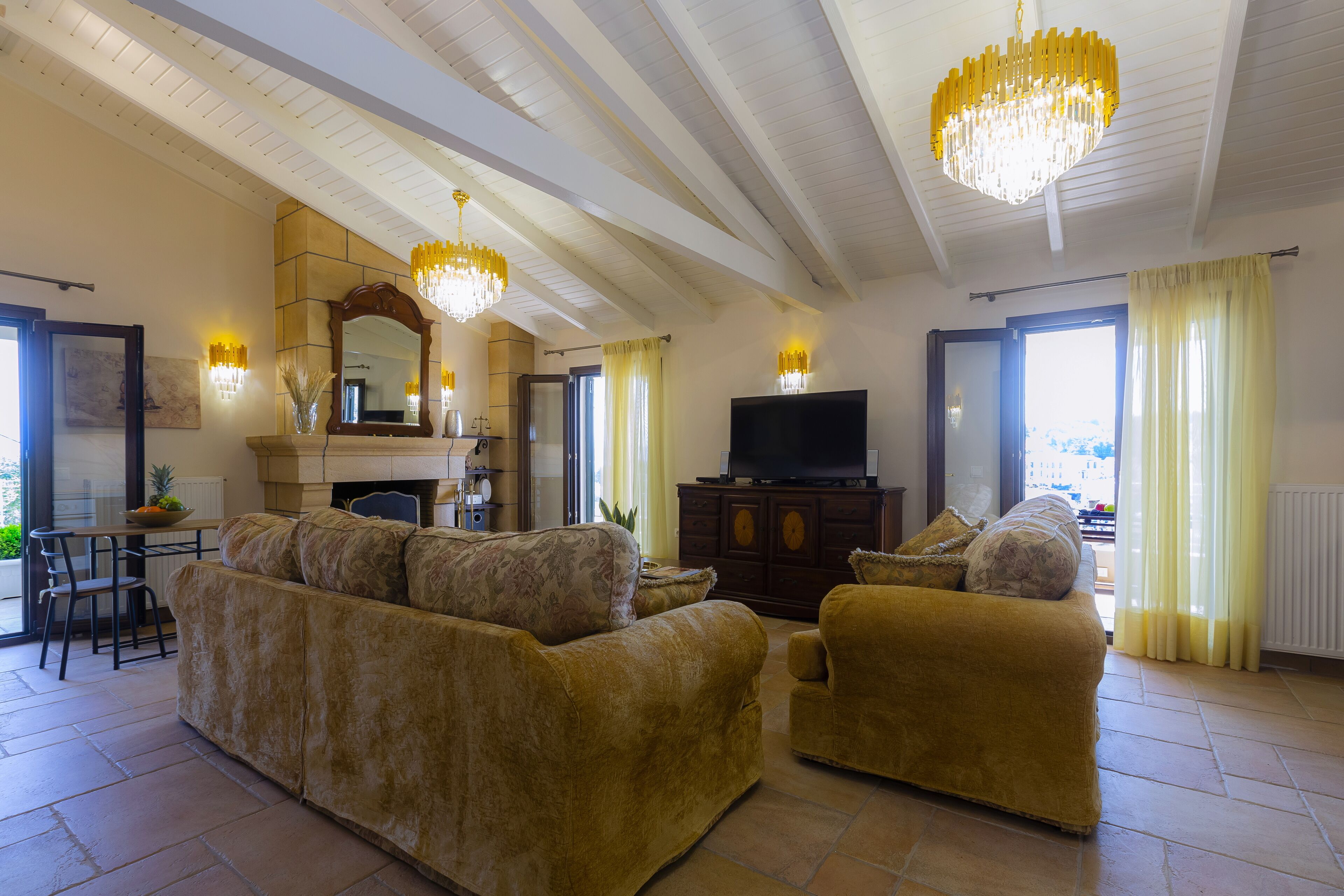 Un salón espacioso con un sofá grande, un sillón más pequeño, una chimenea, un televisor y una araña.