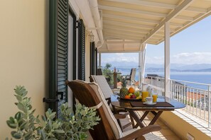 En balkon med et bord dækket til morgenmad, en stol og udsigt til havet.