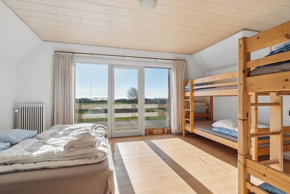 A room with a bed, a bunk bed, a radiator, and a large window with curtains.