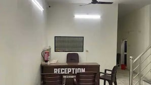 A reception desk with a sign reading "RECEPTION" and "TIME 12:00 NOON". There are two chairs in front of the desk.