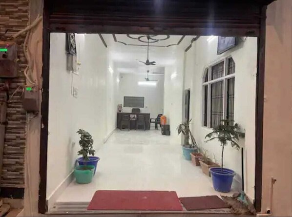 A hallway with a reception desk, potted plants, and a ceiling fan. - SHREE JEE HOME STAY (Faizabad)
