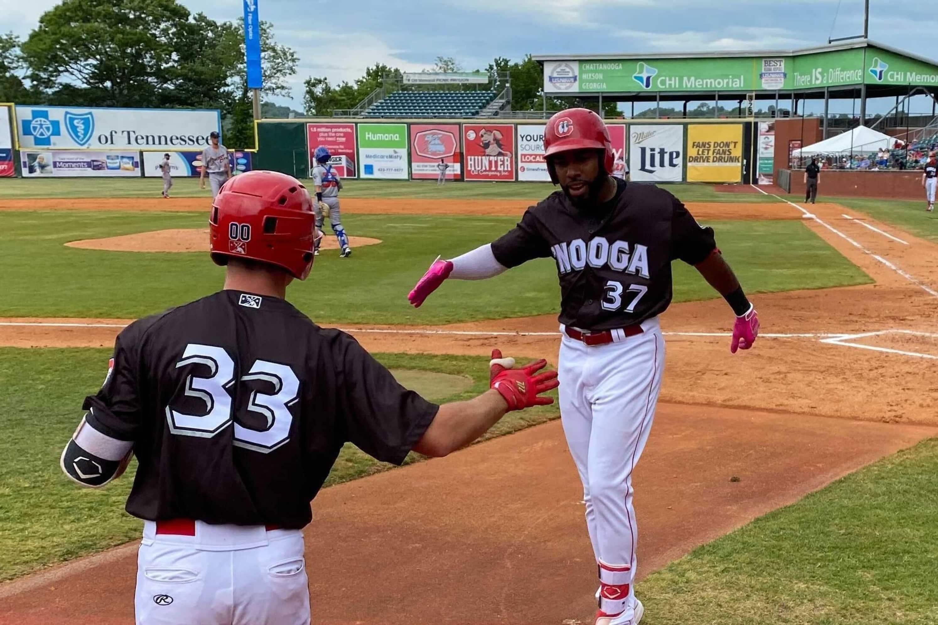 A baseball field with players in black and white uniforms, a pitcher in red, and a catcher in blue.