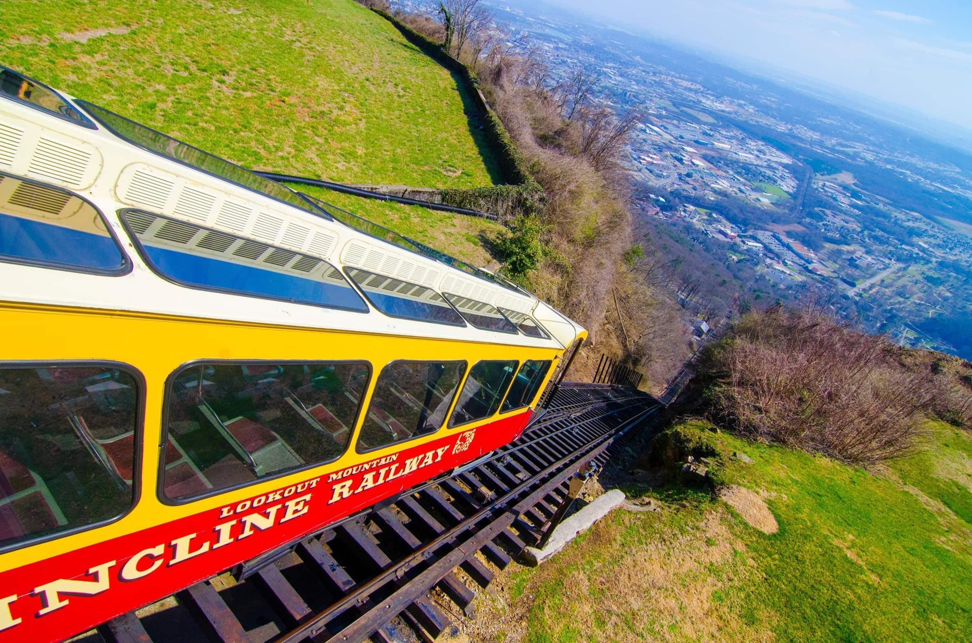 Un chemin de fer de montagne avec un train jaune et rouge, des voies ferrées et une vue sur une vallée.
