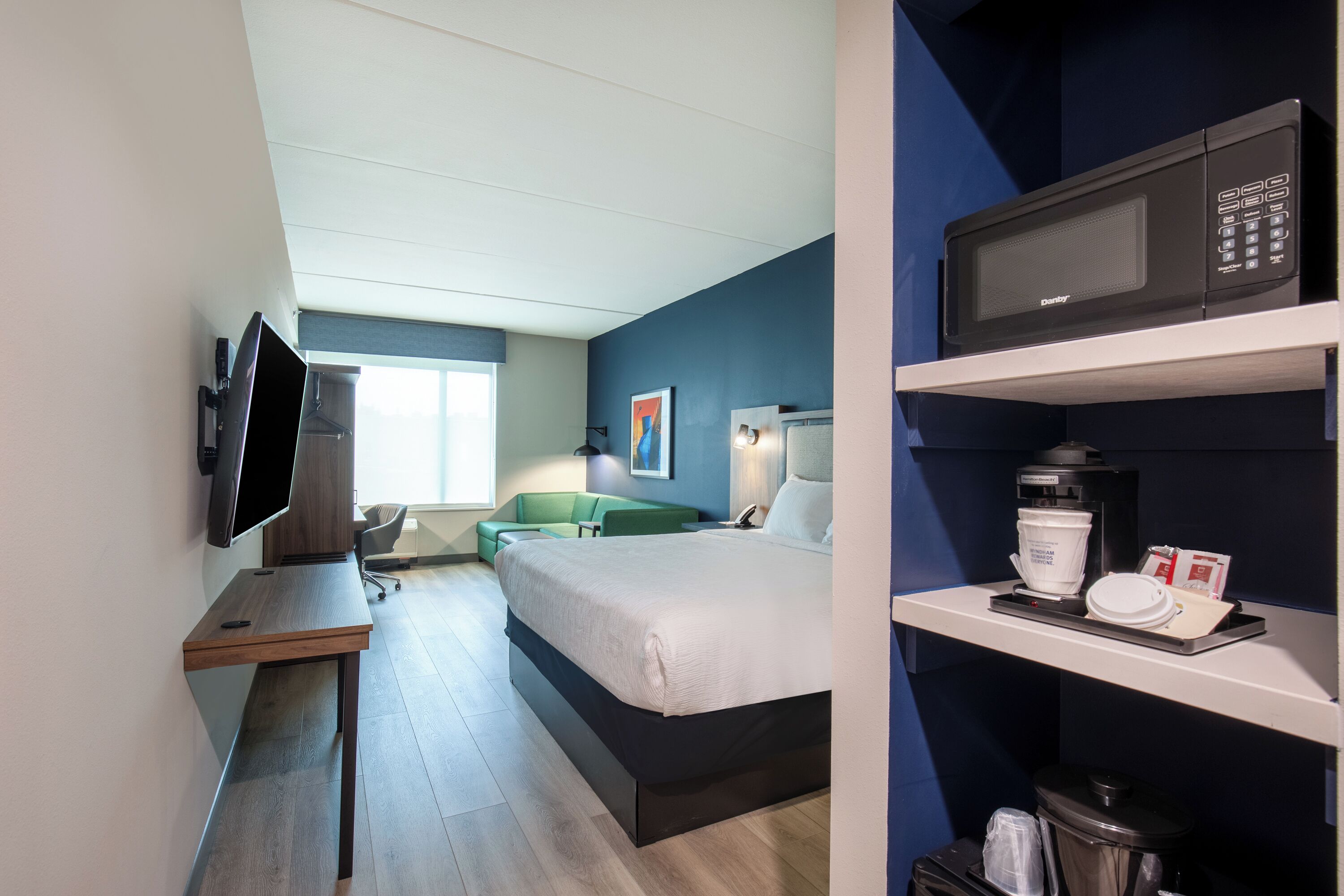 A hotel room with a bed, a desk with a flat-screen TV, a microwave, and a coffee maker.