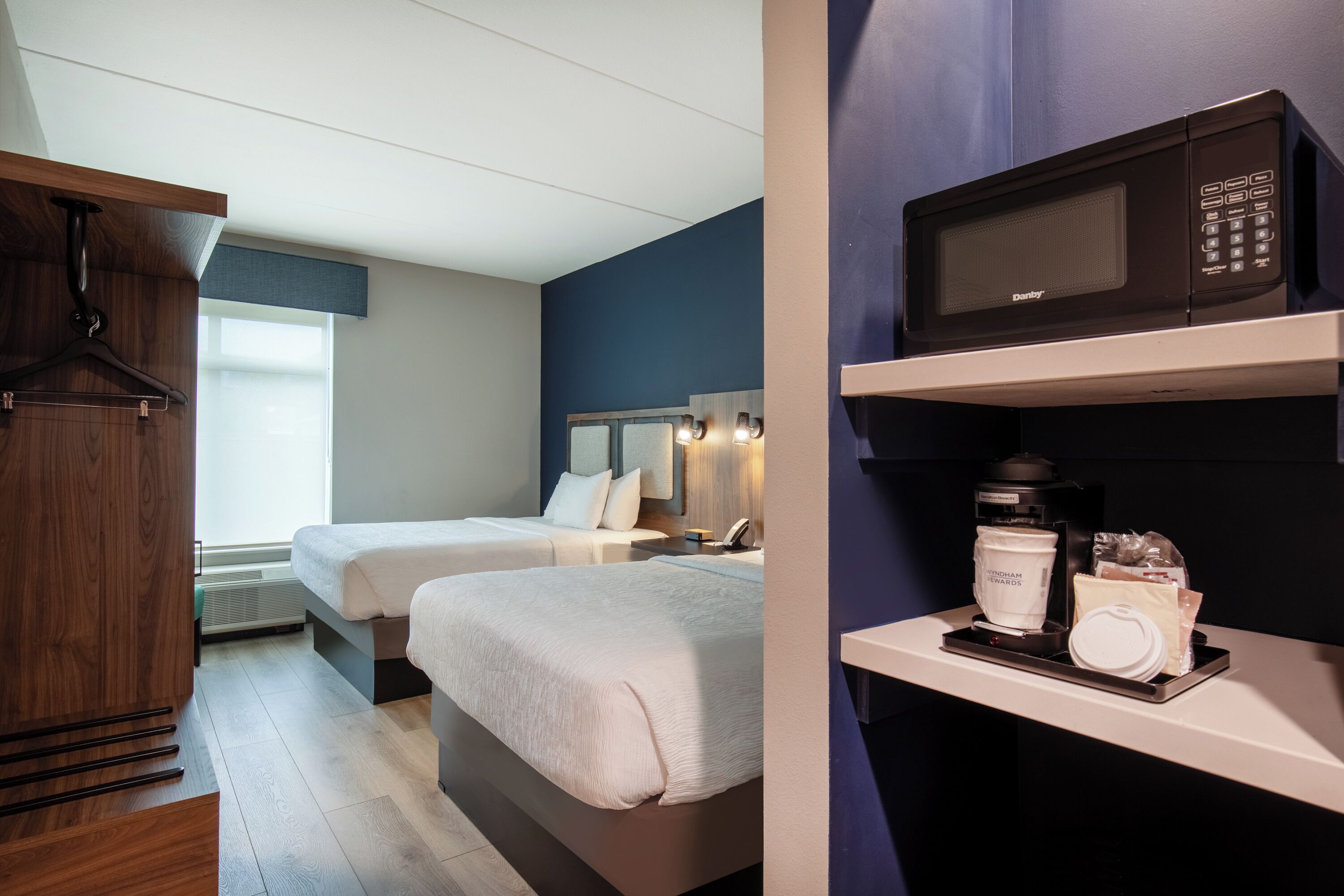 A hotel room with two beds, a wooden wardrobe, a microwave, and a coffee maker on the counter.