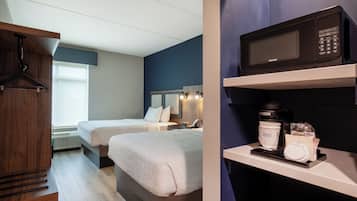 A hotel room with two beds, a wooden wardrobe, a microwave, and a coffee maker on the counter.