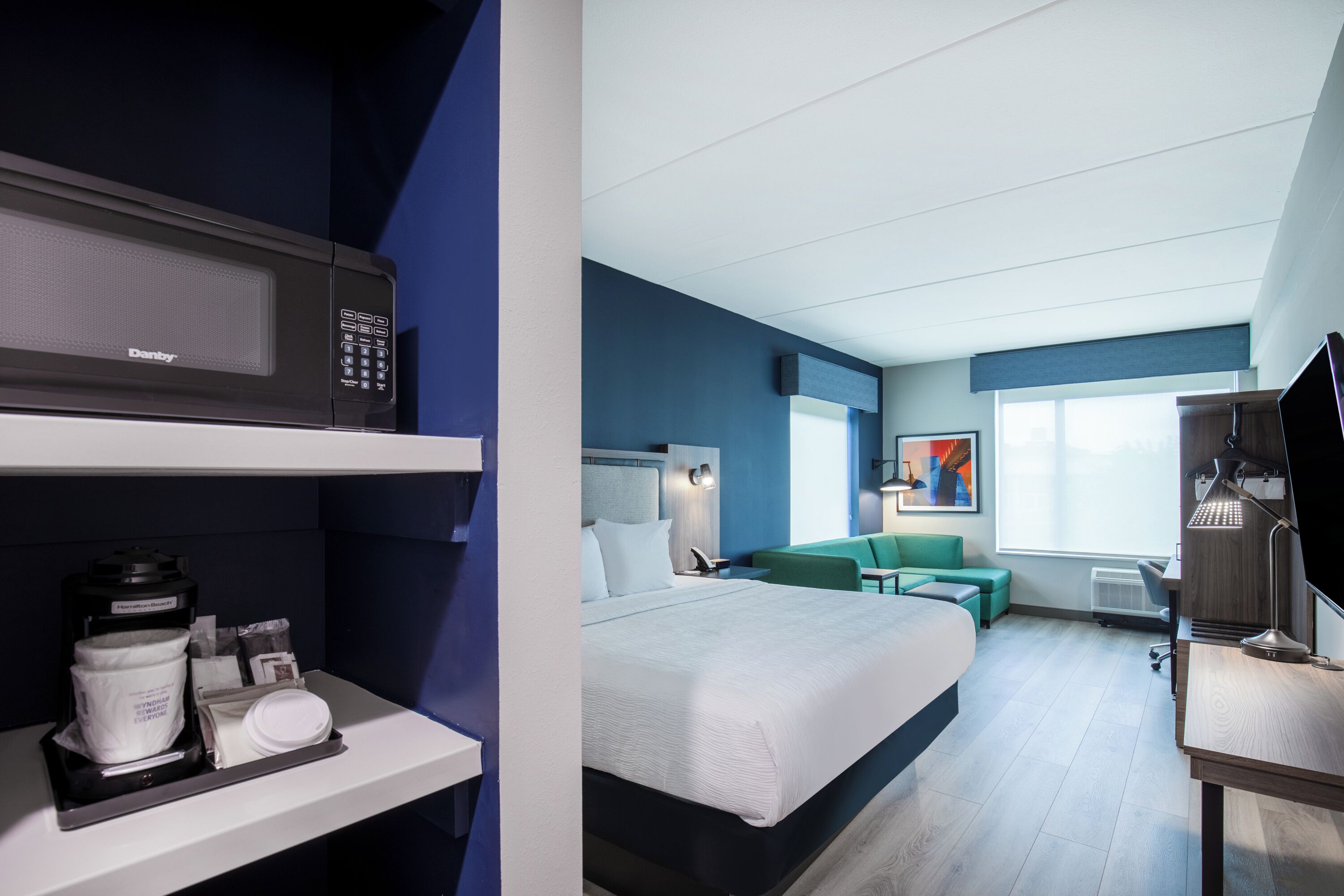 A hotel room with a bed, a desk, a chair, a microwave, and a coffee maker.
