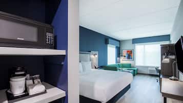 A hotel room with a bed, a desk, a chair, a microwave, and a coffee maker.