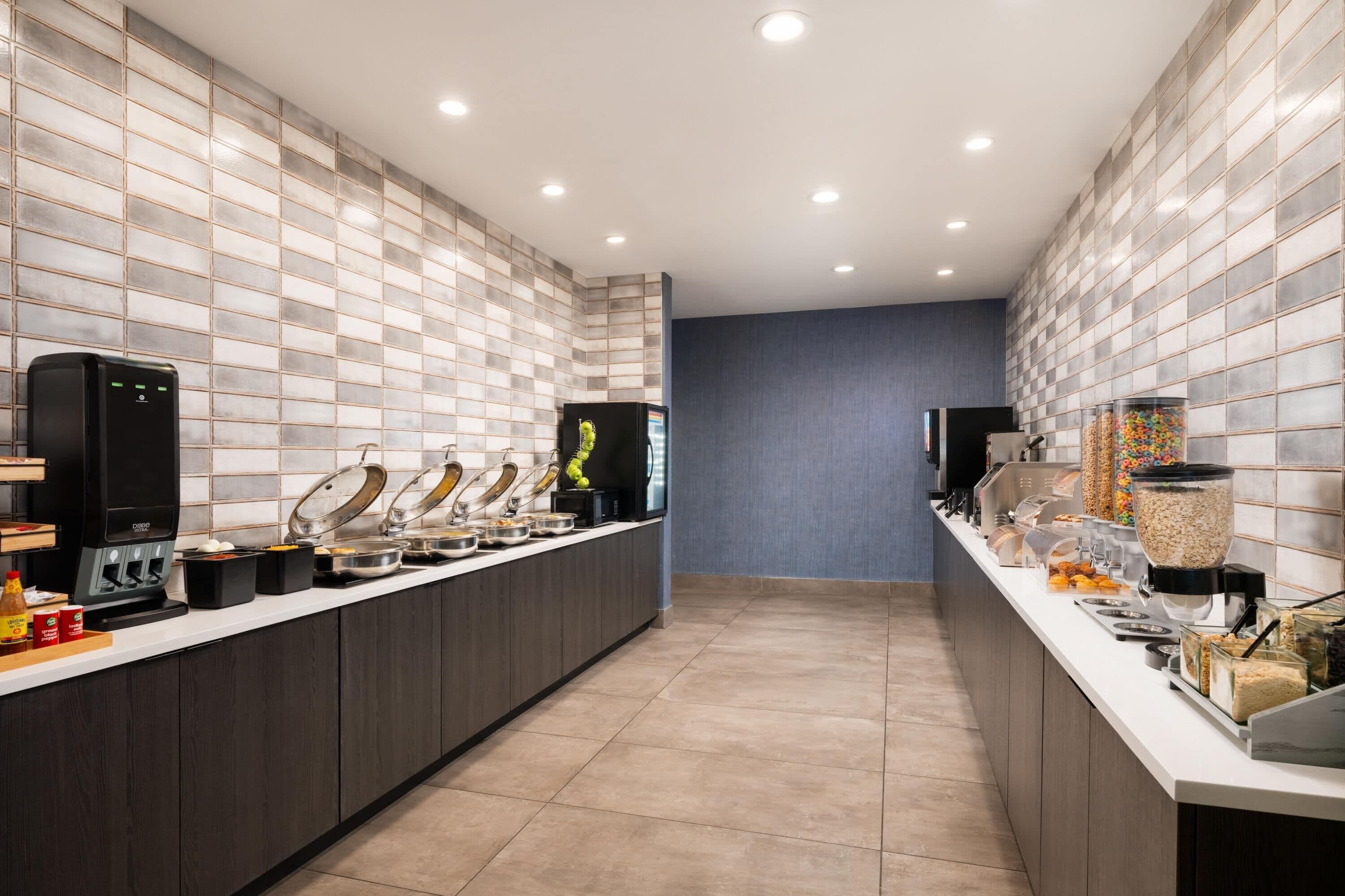 Cozinha moderna com bancada comprida, máquinas de café e diversos dispensadores de alimentos.