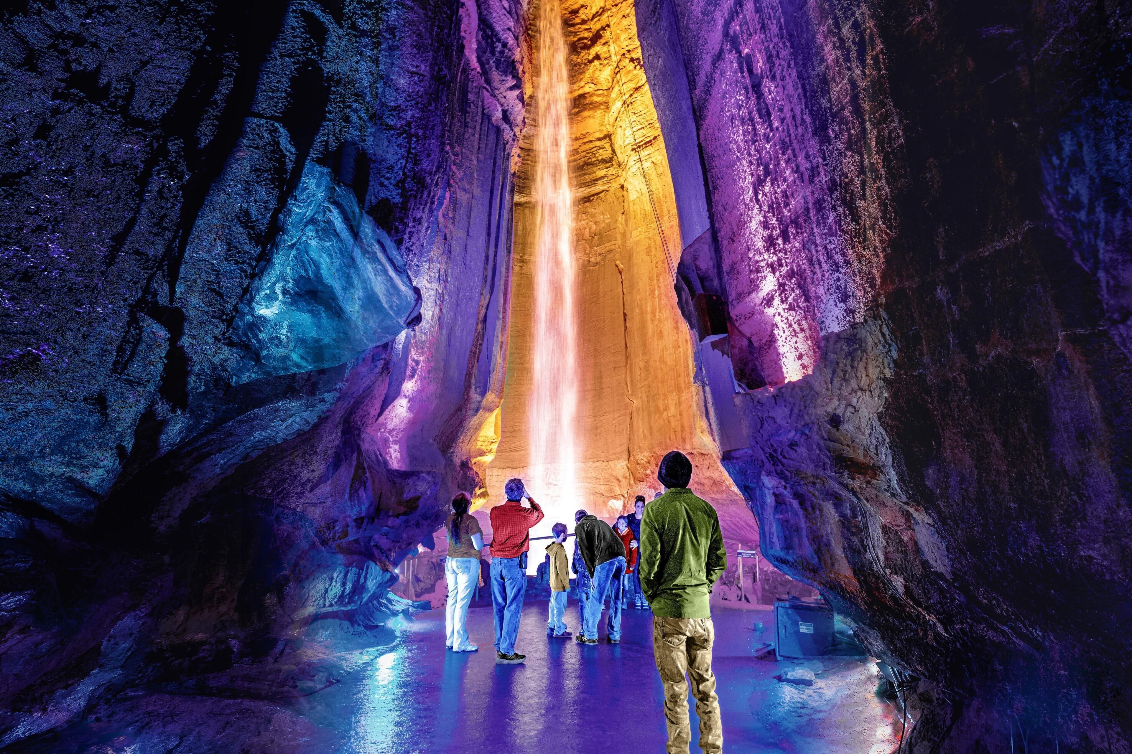 A group of people observing a waterfall in a cave with rocky walls.