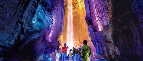 A group of people observing a waterfall in a cave with rocky walls.