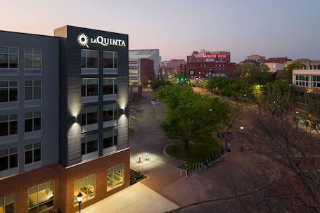 A multi-story building with 'LA QUINTA' signage, a parking lot, and a tree-lined pathway.