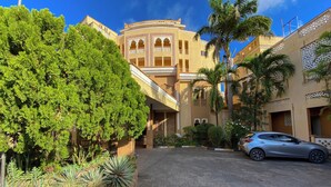 A courtyard with a car parked in front of a building with arched windows and a balcony. - Shanzu Palm Beachfront Apartments (Mombasa)