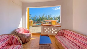 A balcony with wicker furniture, a pool, and a view of buildings and trees. - Shanzu Palm Beachfront Apartments (Mombasa)