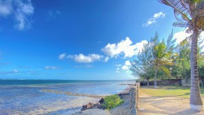 A coastal view with clear blue water, a stone wall, and a grassy area with trees. - Shanzu Palm Beachfront Apartments (Mombasa)